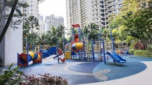 A playground with slides and climbing structures surrounded by tall residential buildings and palm trees. - Holiday Home@Forest City~TV Box~2BR1B 4-6pax 1807 (Gelang Patah)