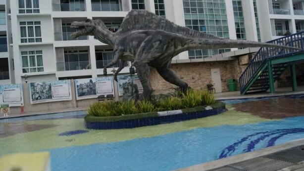 A dinosaur statue in a pool area with a building in the background.