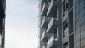 A modern building with a swimming pool in the foreground, featuring multiple balconies and large windows.