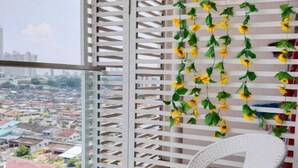 A balcony with a white wicker chair, a white lattice partition, and a view of a cityscape.