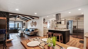 A modern kitchen with a central island, stainless steel appliances, and a dining area with wooden flooring and a large table. - Breathtaking Lake Views | Private Dock, Fire Pit & Chef’s Kitchen (Hauser)