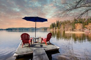 A dock with two red Adirondack chairs and a table under a blue umbrella.