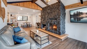 A cozy living room with a stone fireplace, wooden ceiling beams, and a modern sofa. - Breathtaking Lake Views | Private Dock, Fire Pit & Chef’s Kitchen (Hauser)