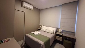 Un dormitorio con cama, mesitas de noche, escritorio y un cubo de basura.