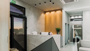 Una zona de recepción moderna con un mostrador de mármol, un panel de pared de madera y un área de estar con sofá y mesa de centro.