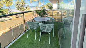 En balkon med et lille bord og stole, en plantekasse og udsigt til en gade med biler.