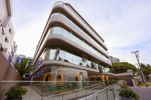 A modern multi-story building with a curved facade, large windows, and a glass staircase leading to an outdoor seating area. - Setai Yacht Luxo - By Almare Flats (Joao Pessoa)