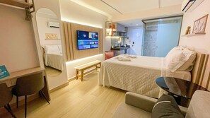 Habitación de hotel con cama, escritorio, silla, televisor y baño visible a través de una puerta abierta.