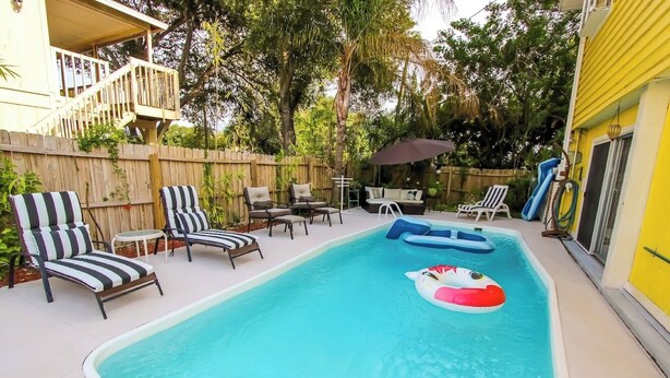 A backyard with a swimming pool, lounge chairs, a deck, and a covered seating area. - The Sunburst Oasis  (Palm Harbor)