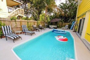 Un jardin avec une piscine, des chaises longues, une terrasse et un espace salon abrité.