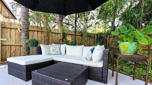 A wicker sectional sofa with cushions, a matching ottoman, and a small table with a potted plant. - The Sunburst Oasis  (Palm Harbor)