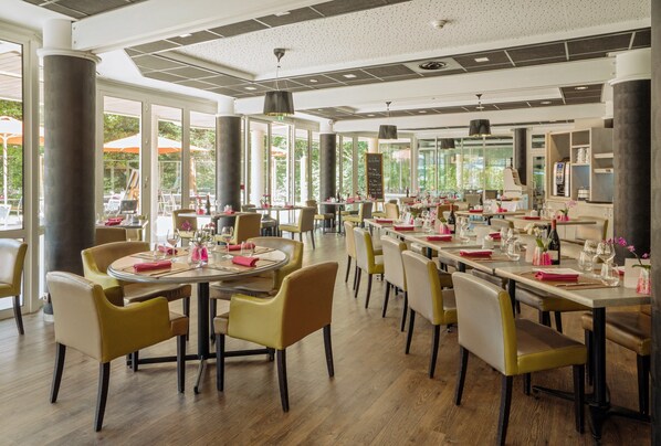 A spacious restaurant with round tables and yellow chairs, large windows, and a modern ceiling design.