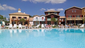 A swimming pool with lounge chairs and a row of buildings in the background. - Duplex 8p • Réserve naturelle | Piscine incluse (Le Teich)