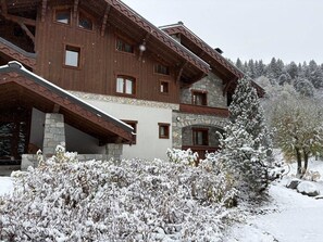 A multi-story building with a stone facade and wooden balconies, surrounded by snow-covered vegetation.