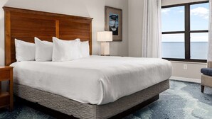 Hotelkamer met een groot bed, een houten hoofdbord, een nachtkastje met een lamp, een stoel en een raam met uitzicht op zee.
