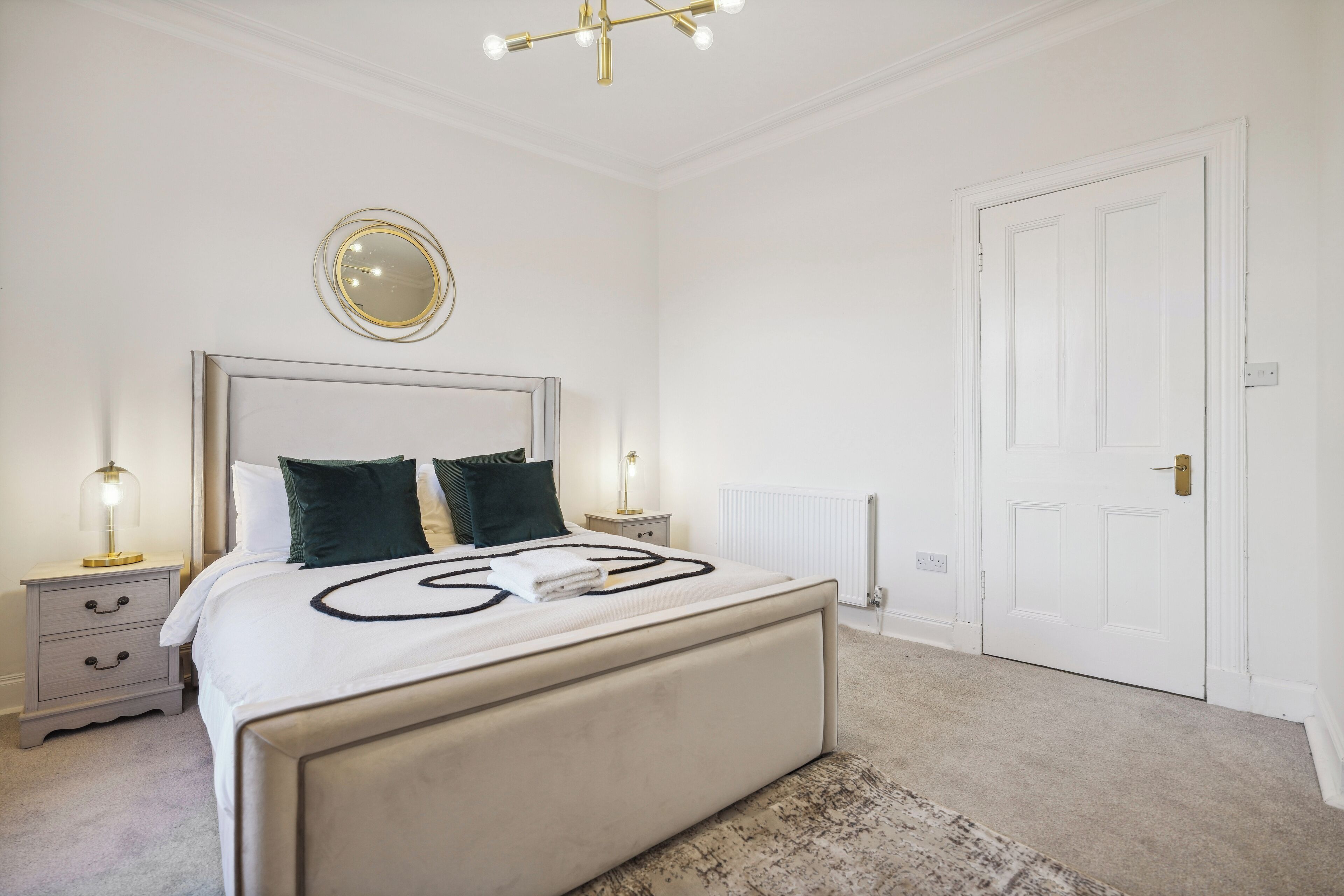 A bedroom with a large bed, bedside tables, a mirror, and a door.