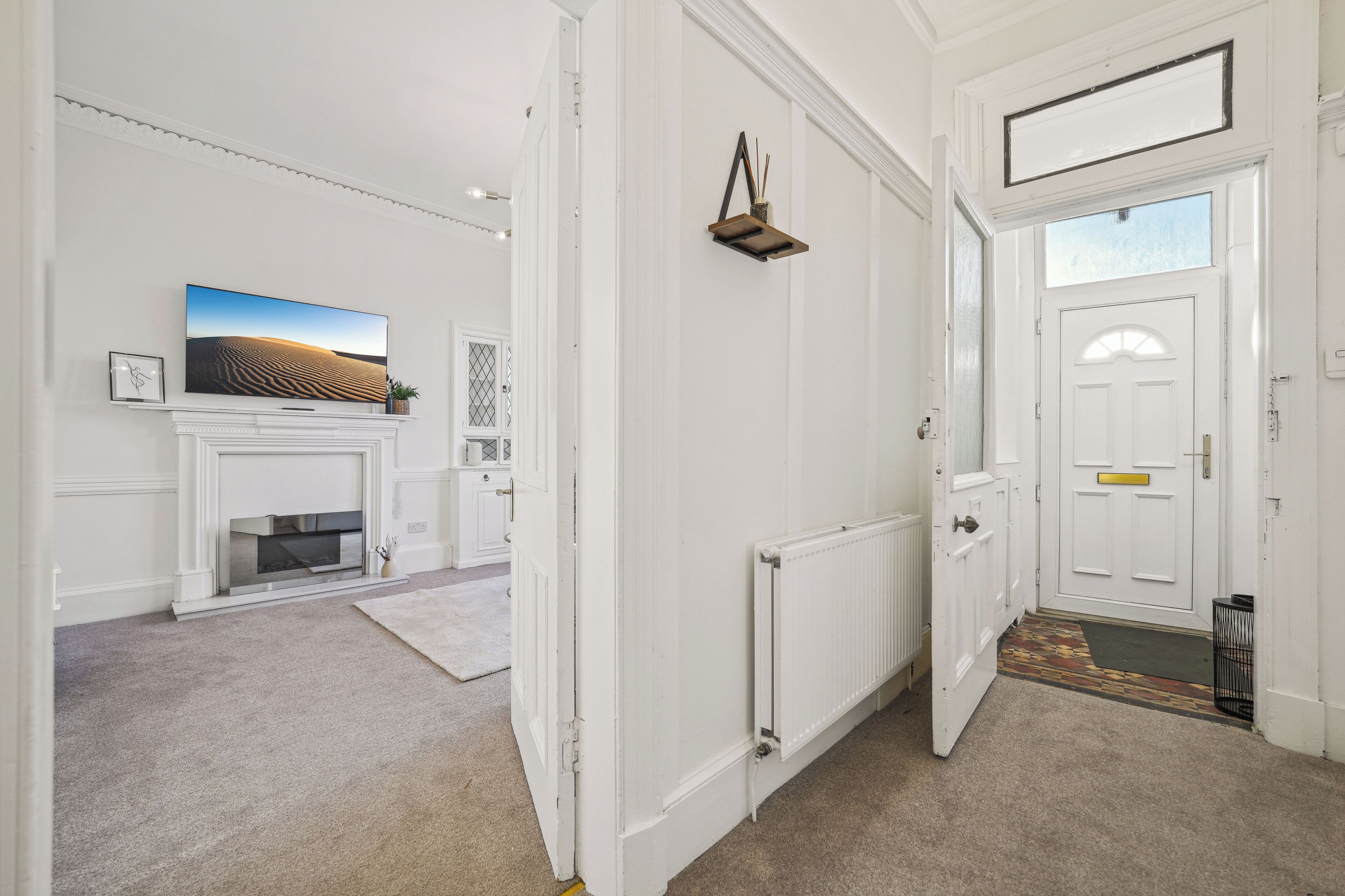 A hallway with a white fireplace, a mounted TV, and a door with a doormat.