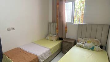 Une chambre avec deux lits, une fenêtre avec des rideaux, une table de chevet et un tapis à motifs.