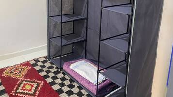 Une pièce avec un meuble de rangement gris adossé à un mur, un tapis à motifs sur le sol et une porte partiellement visible.