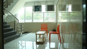 Un intérieur moderne avec un escalier, deux fauteuils orange, une petite table et de grandes fenêtres équipées de climatiseurs.
