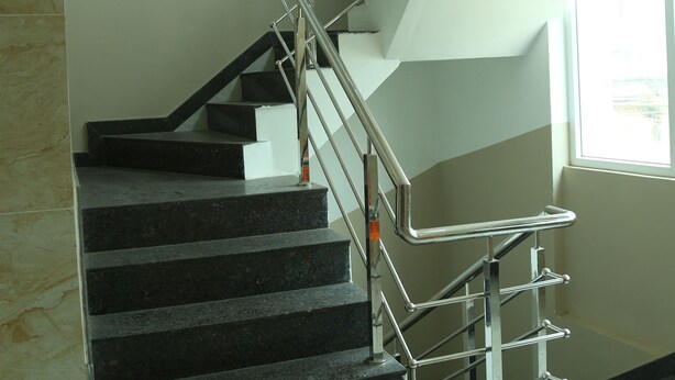Un escalier avec des rampes en métal et des marches noires, situé dans un bâtiment.