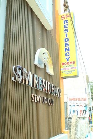 Une enseigne d’hôtel avec les inscriptions « SM RESIDENCY » et « STAY UNIQUE », un numéro de téléphone et l’adresse située à Baniyan Bazaar.