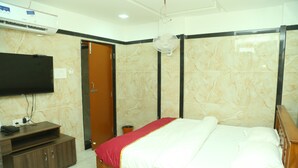 Une chambre à coucher avec un lit, un téléviseur fixé au mur, une armoire en bois et un ventilateur de plafond.