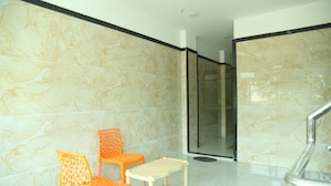 Une salle de bain aux murs recouverts de marbre, dotée d’une douche en verre et de deux chaises orange.