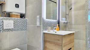 Et moderne badeværelse med toilet, vaskebord med spejl og en bruseafdeling.