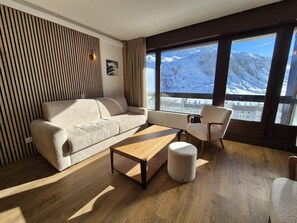 A modern living room with a sofa, a coffee table, and a chair, with a large window offering a mountain view.