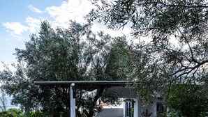 A house with a paved patio, a pergola, and a garden area with trees and shrubs. - Maison De Yaya at Heraion Lagoon (Loutraki-Agioi Theodoroi)
