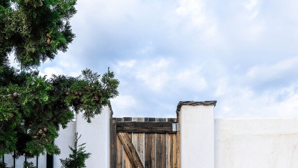 A set of stone steps leading to a wooden gate with a diagonal brace, flanked by white walls and a tree. - Maison De Yaya at Heraion Lagoon (Loutraki-Agioi Theodoroi)