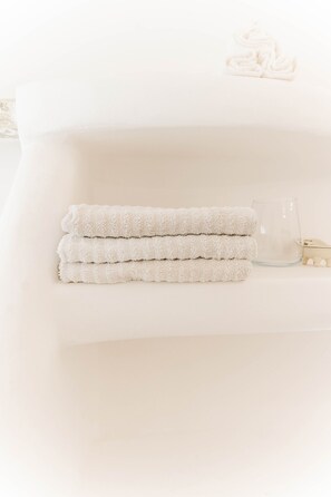 A neatly folded set of towels stacked on a white surface, accompanied by a clear glass and a small wooden object.