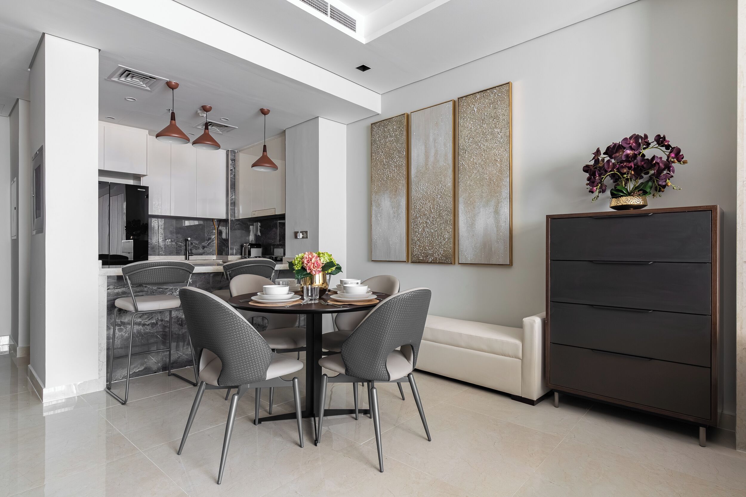A modern kitchen with white cabinets, a dining area with a marble island, and pendant lighting.