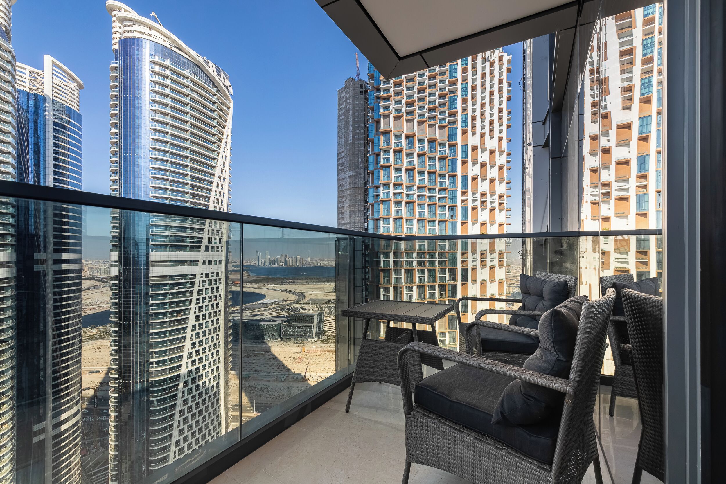 A balcony with wicker furniture, a glass railing, and a view of high-rise buildings.