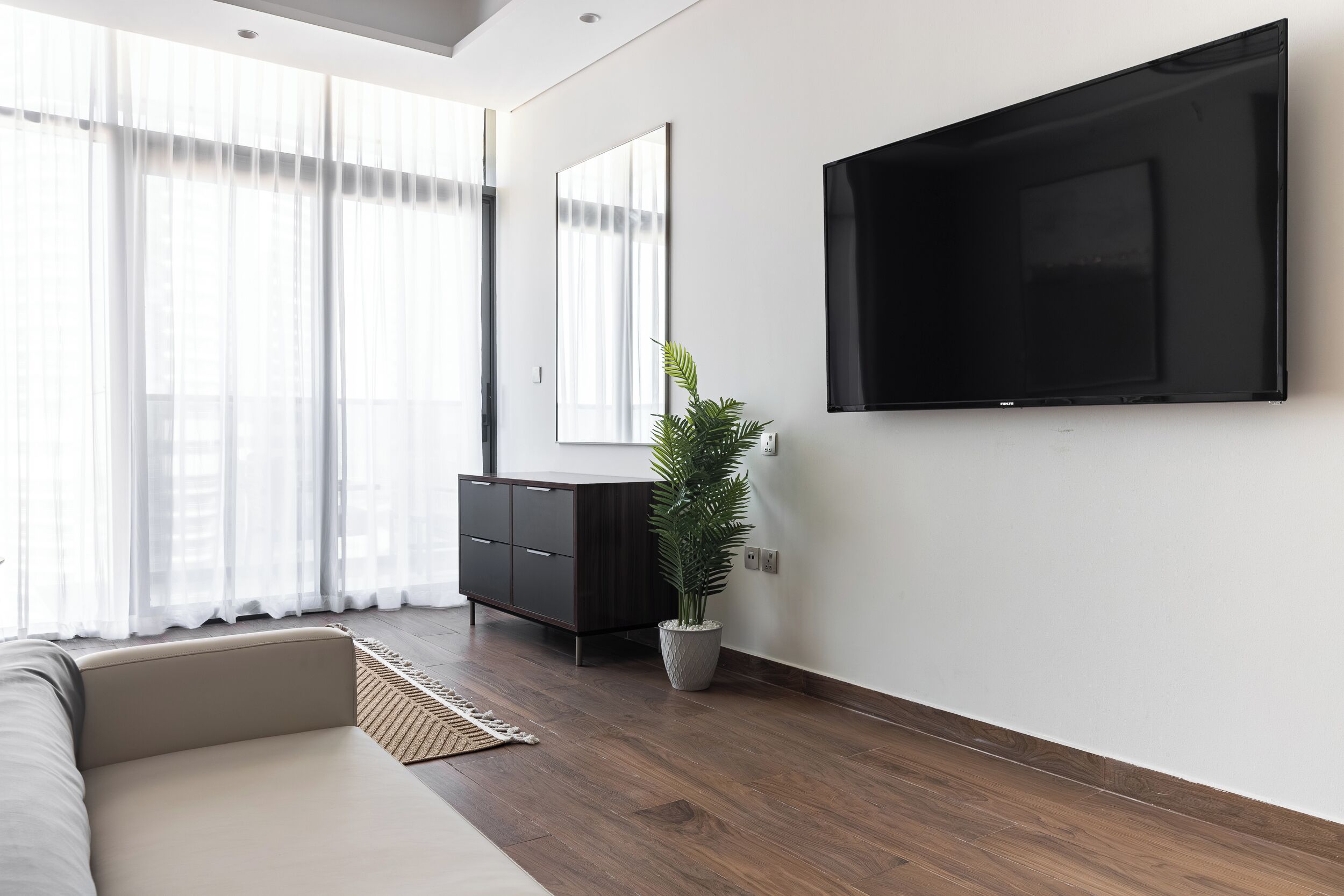 Een moderne woonkamer met een bank, een donker houten kast, een potplant en een tv aan de muur.