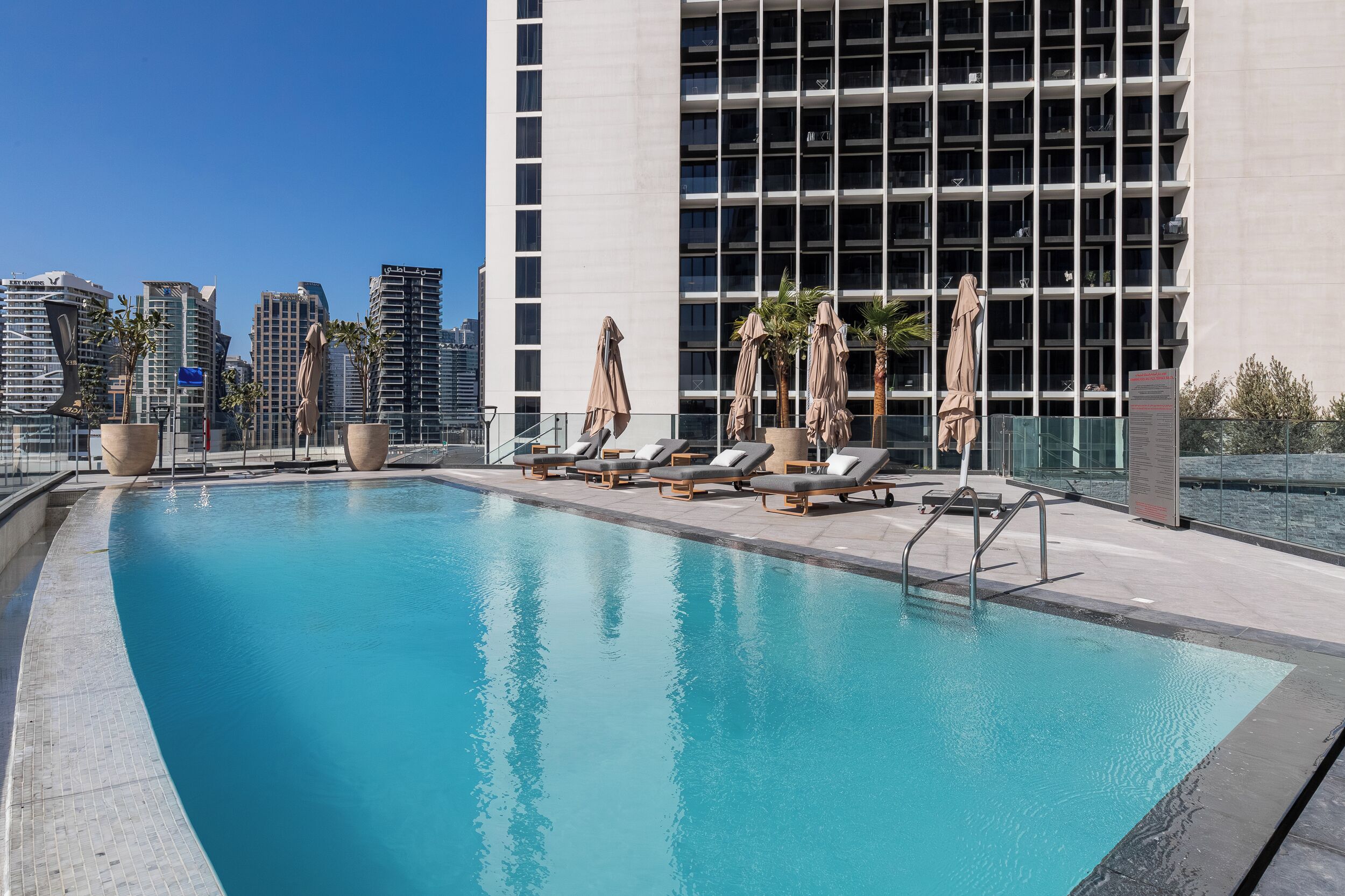 A rooftop pool with lounge chairs and umbrellas, surrounded by high-rise buildings.