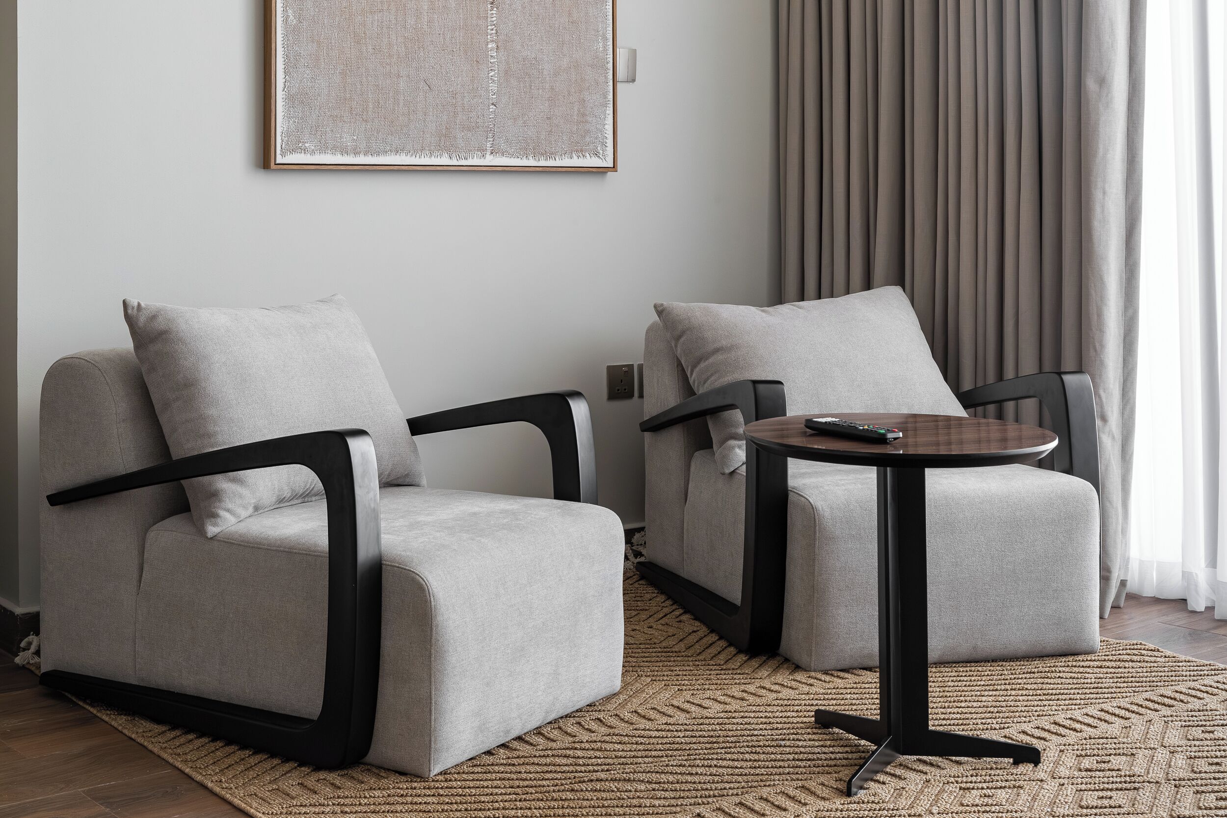 Un salon moderne avec deux canapés gris, une table basse ronde en bois et un tapis à motifs.