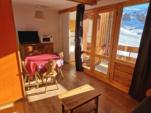 Ein Essbereich mit einem Tisch für vier Personen, Holzboden und Blick auf eine verschneite Landschaft durch eine Glastür.