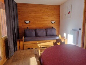 Ein gemütliches Zimmer mit einer Holzwand, einer Couch mit Kissen, einem Holztisch und einem Bett mit roter Bettdecke.
