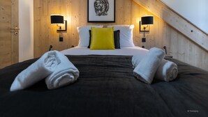 A bedroom with a wooden ceiling, a bed with white and yellow pillows, two wall-mounted lamps, and a framed picture on the wall. - Chalet in Chantemerle With Sunny Ski Slopes (Saint-Chaffrey)