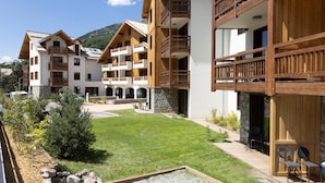 A multi-story hotel with wooden balconies, a well-maintained lawn, and a mountainous backdrop. - Chalet in Chantemerle With Sunny Ski Slopes (Saint-Chaffrey)