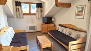 A cozy loft-style room with a wooden bed, a sofa, a small wooden table, and a TV.