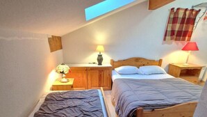 A small, cozy bedroom with two single beds, a wooden headboard, a nightstand with a lamp, and a skylight above. - 100m from ski slopes, 2nd floor, balcony, ski locker, 90m², Valfréjus (Valfréjus)