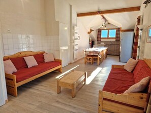 A cozy living room with two wooden sofas and a coffee table, a kitchen area with a dining table, and a small kitchenette.