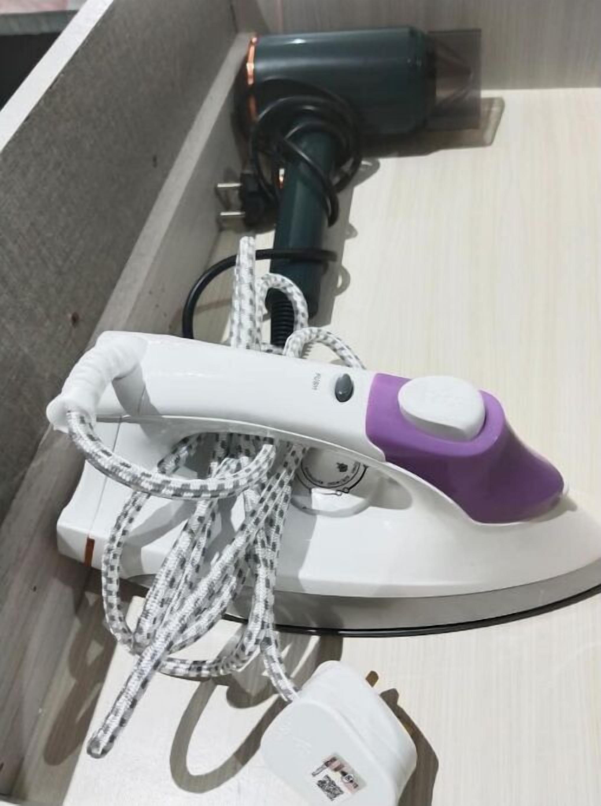 A white and purple iron with a cord, placed on a wooden surface.