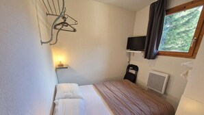 A small, neatly arranged bedroom with a single bed, a bedside table, a lamp, a TV, and a window with a view of trees. - 100m from ski slopes, 2nd floor, balcony, ski locker, 48m², Valfréjus (Valfréjus)