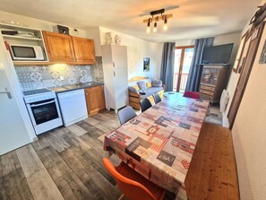 Eine kompakte Küche mit Mikrowelle, Backofen und Geschirrspüler, ein Esstisch mit Tischdecke und ein Sofa im angrenzenden Wohnbereich.