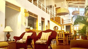 A spacious living area with wicker furniture, a staircase, and a large window providing natural light. - Beautiful Oceanfront Home in Zorritos - Just 2 Hours from Tumbes Airport (tumbes)