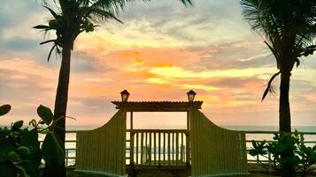 Une porte en bois qui mène à une plage bordée de palmiers, avec un coucher de soleil en arrière-plan.